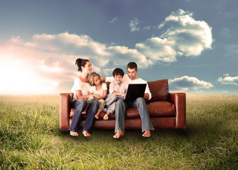 Happy family in the couch using the laptop in a sunny field in the countryside
