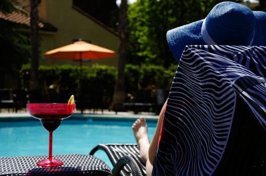 Girl in blue hat with coctail drink by the pool
