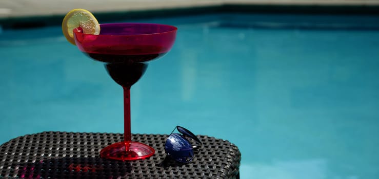 Coctail and sunglasses on summer wicker chair by the pool