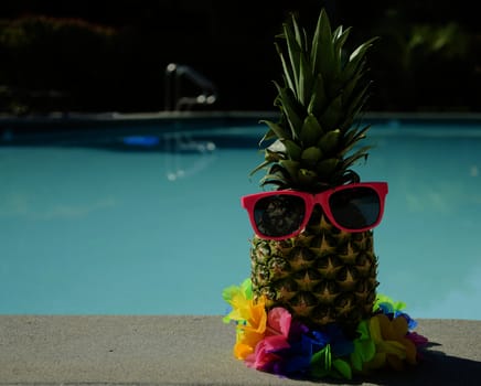 Funny pineapple in sunglasses by the pool