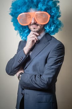 funny businessman with big orange glasses and blue wig on gray background