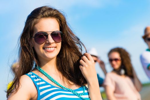 stylish young woman in sunglasses on the background of blue sky and friends