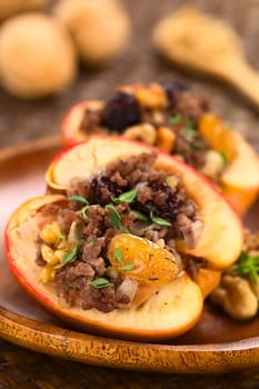 Savory baked apple filled with mincemeat, raisins, sultanas, onion and walnut, sprinkled with fresh thyme leaves on top with walnuts in the back (Selective Focus, Focus on the filling in the front)   