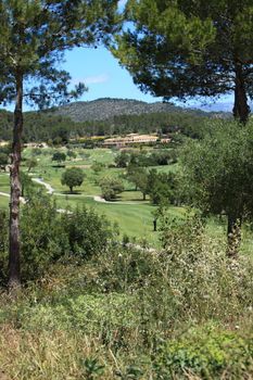 View between two trees of the manicured fairways of a rural golf course surrounded by forested hills
