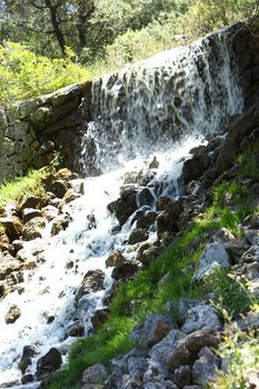 Flowing mountain stream cascading over a shallow rocky ledge, close up view in woodland