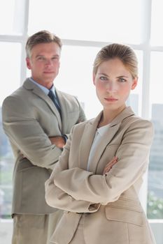 Serious business people standing with arms crossed in their office