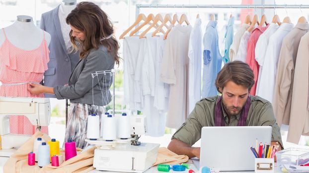 Fashion designers working on laptop and measuring dress