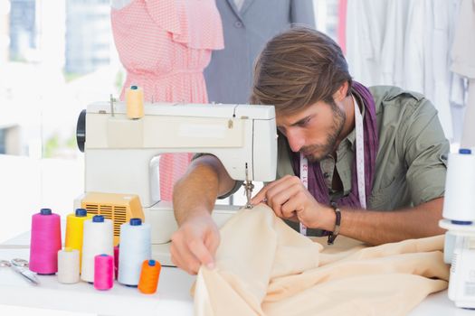 Handsome fashion designer sewing with a sewing machine