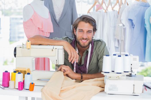 Smiling fashion designer leaning on sewing machine