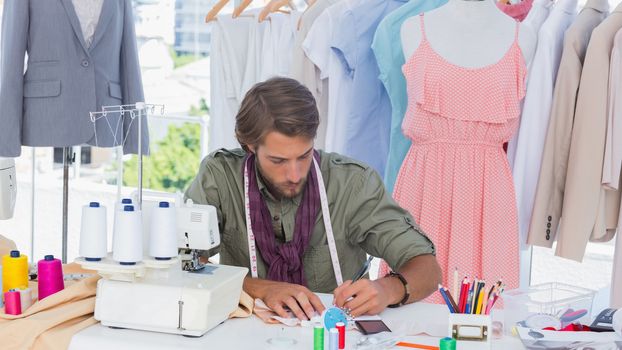 Fashion designer drawing on a desk in front of clothes