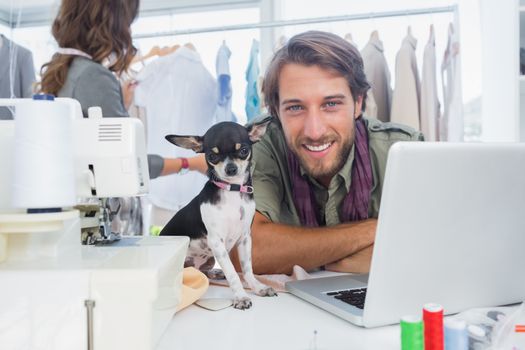 Smiling fashion designer with his chihuahua sits on desk
