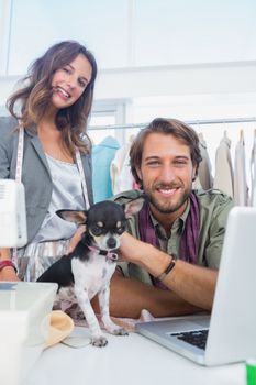 Two fashion designers smiling to the camera with a chihuahua