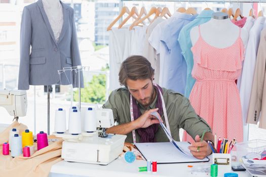 Fashion designer sitting behind a desk with spools of thread and sewing machine