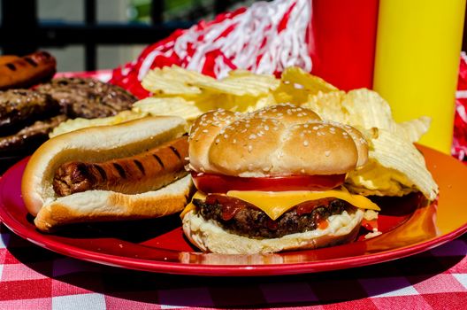 Tailgate party with cheeseburger, hot dog, potato chips, pom poms, hamburger patties, hot dog wieners,  and mustard and ketchup bottles.  