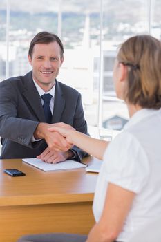 Businessman giving a handshake to a job applicant in his office