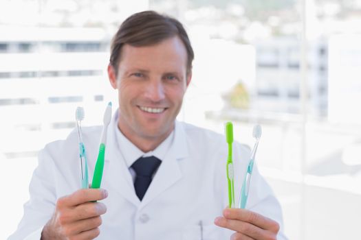 Smiling doctor holding two toothbrushes in his office
