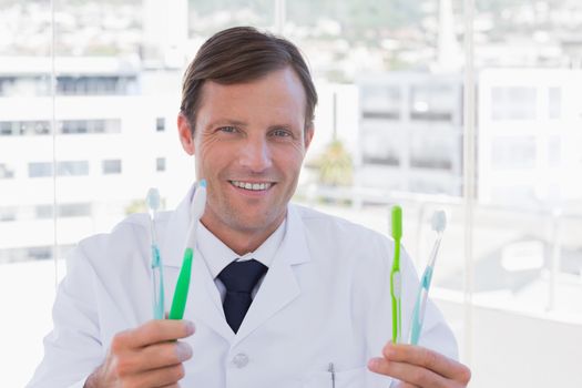 Happy doctor holding two toothbrushes in his office