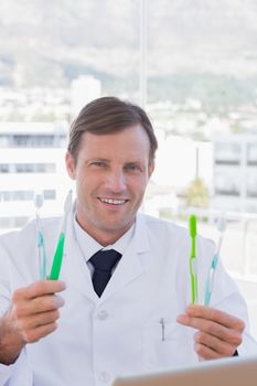 Cheerful doctor holding two toothbrushes in his office