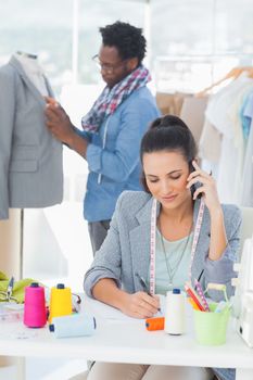 Attractive fashion designer calling while her colleague adjusting blazer on a mannequin