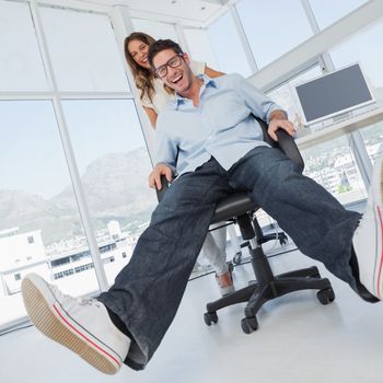 Smiling designers having fun with on a swivel chair in their office