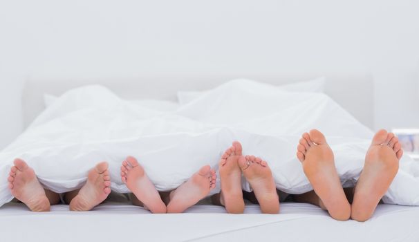 Family showing their feet while lying on bed