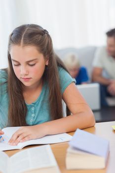Girl doing her homework with her family behind her
