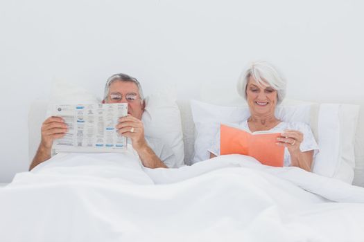 Mature people reading newspaper and book in bed