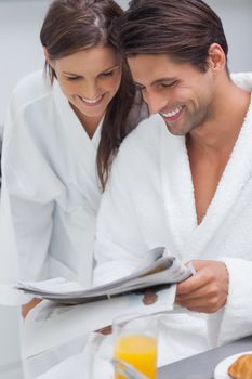 Lovely couple wearing bathrobes and reading newspaper