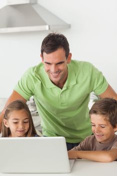 Man and his children using a laptop together in the kitchen