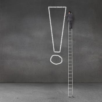 Businessman writing an exclamation mark on a grey wall