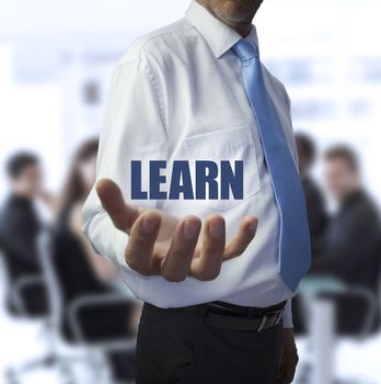 Smart businessman holding the word learn in front of a business team
