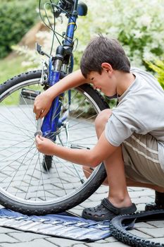 Teenager repairing his bike, using spanner to change broken tyre, outdoor shoot