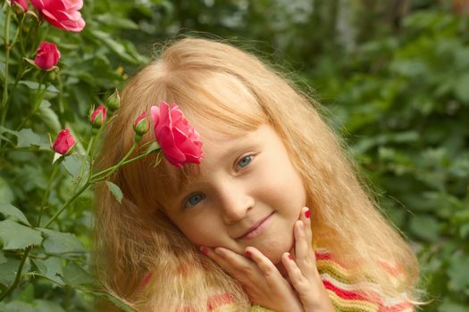 Beautiful little Caucasian girl in park near the rose bush