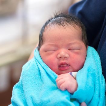 Newborn Asian baby girl smiling and fall asleep in father's arms, inside hospital room