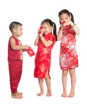 Asian children peeking into red packet during Chinese New Year, with traditional Cheongsam full length standing isolated on white background.