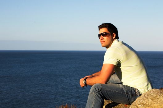 Sexy man wearing sunglass enjoying the sun on cliff seaside