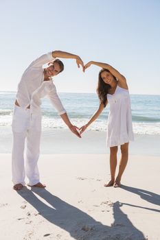 Romantic couple forming heart shape with arms at the beach
