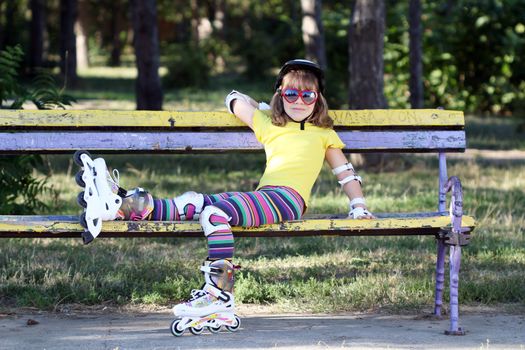 little girl with roller skates and helmet sitting on bench