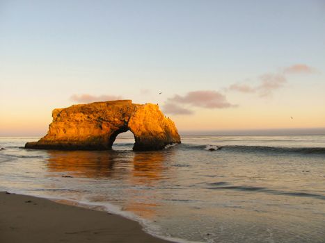Arch rock formation on ocean beach during sunset