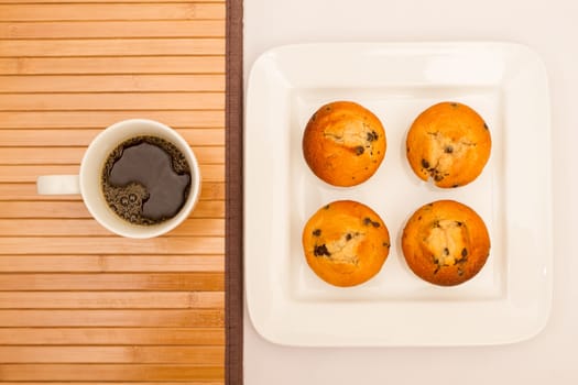 Vanilla with chocolate chips Muffins on a white plate with  a cup of coffee
