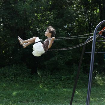 Happy little girl riding on a swing in the park