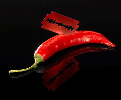 studio shot of a sharp razor blade and red hot chili in dark reflective back
