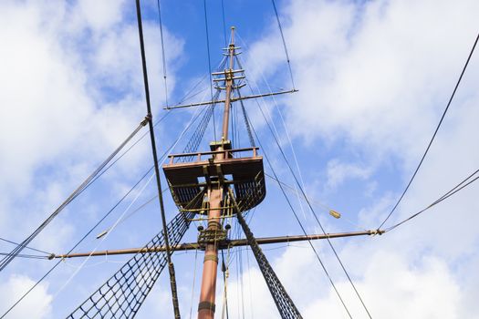 Marine rope ladder, mast and ropes of a classic sailboat against blue sky.