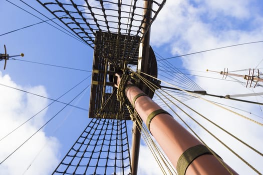 Marine rope ladder, mast and ropes of a classic sailboat against blue sky.