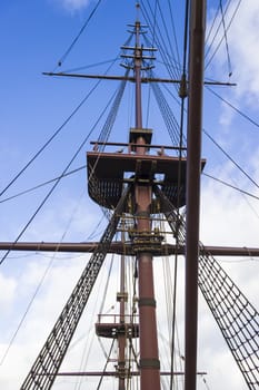 Marine rope ladder, mast and ropes of a classic sailboat against blue sky.