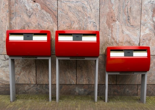 Three red public mailboxes with two slots, common in the Netherlands