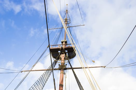 Marine rope ladder, mast and ropes of a classic sailboat against blue sky.