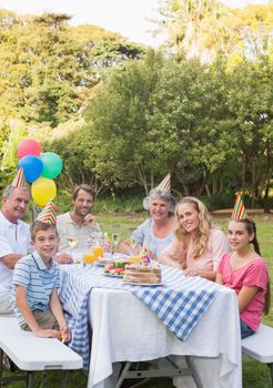 Happy family smiling at camera at birthday party outside at picnic table