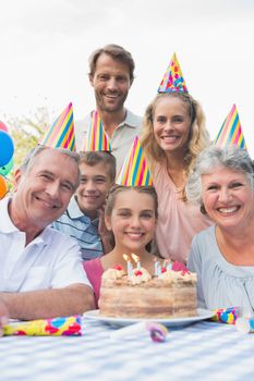 Happy extended family at birthday party smiling at camera outside at picnic table