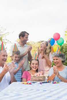 Cheerful extended family clapping for little girls birthday outside at picnic table